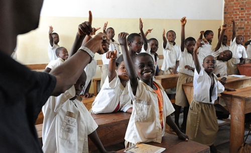 Das Bild zeigt eine afrikanische Schulklasse. Ein Junge lächelt in die Kamera und zeigt auf.