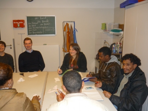 Flüchtlinge und eine Sprachlehrerin sitzen am Tisch