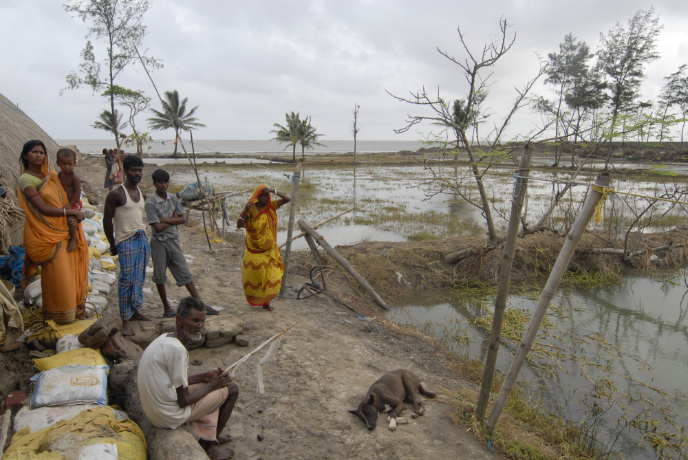 Mehrere Menschen in Indien neben ihren überfluteten Feldern.
